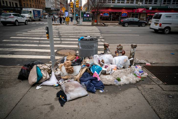 Trash piled up around a New York City trashcan on a corner.